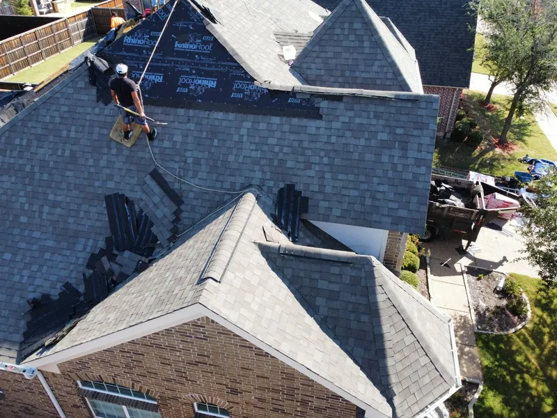Roofer on a steep gray shingle roof installing new shingles on a brick two-story home