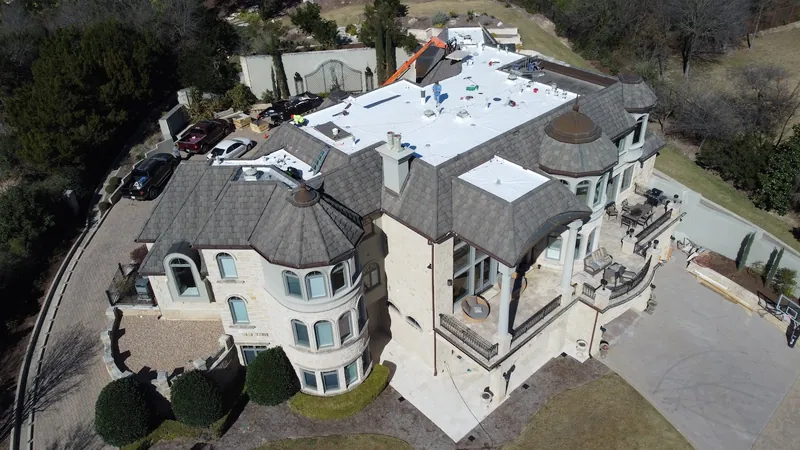 Drone view of a large home with white flat roof sections and a gray shingle roof